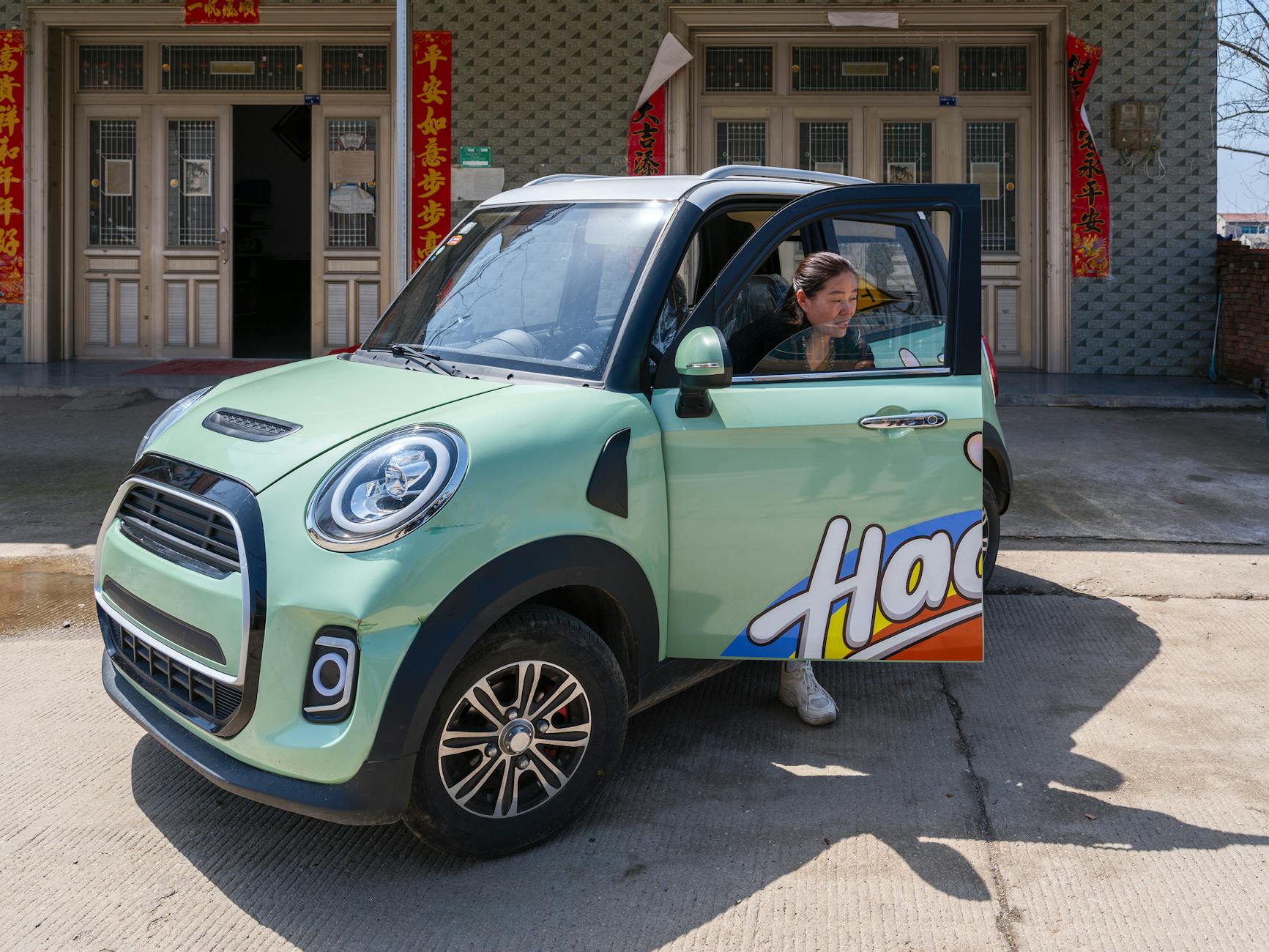 Kobieta wysiada z kolorowego mikrosamochodu elektrycznego w małym mieście